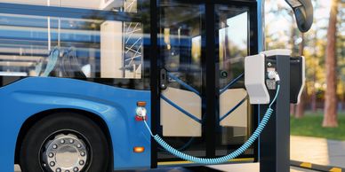 Blue electric bus charging at a station with a coiled cable connected.