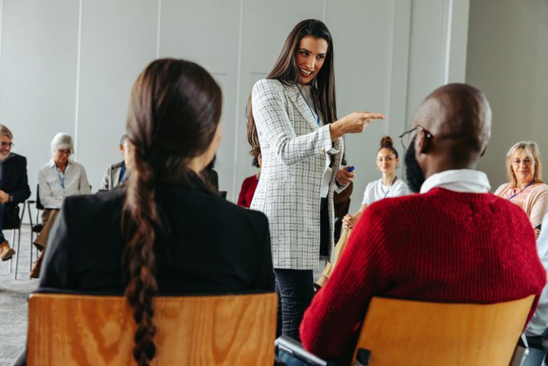 Woman leading a group discussion with diverse participants seated in a meeting room, fostering engagement and communication.