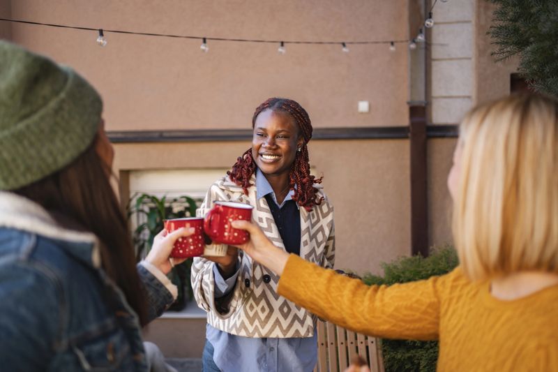 Three diverse women enjoying a relaxing moment, toasting with mugs in a cozy backyard setting