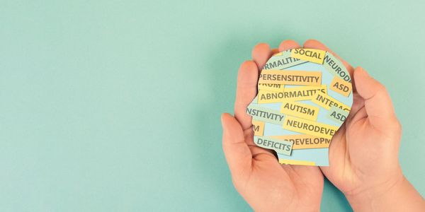 Hands holding a paper cutout of a head with autism-related words.