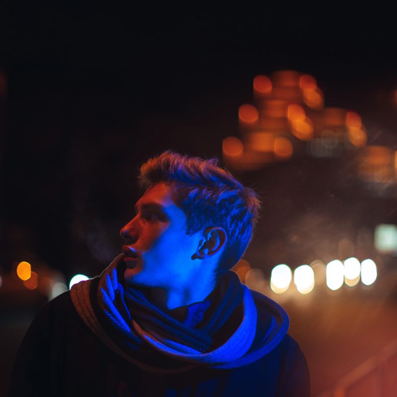 Young man posing under vibrant neon lights with futuristic streaks and a dramatic glow. Ideal for urban, fashion, and creative photography projects with a modern aesthetic.