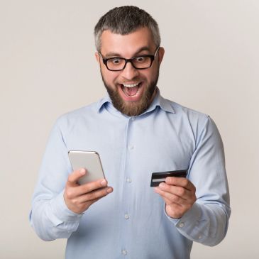Man excitedly looking at phone holding a credit card.