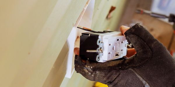 A gloved hand installing an electrical outlet into a wall.