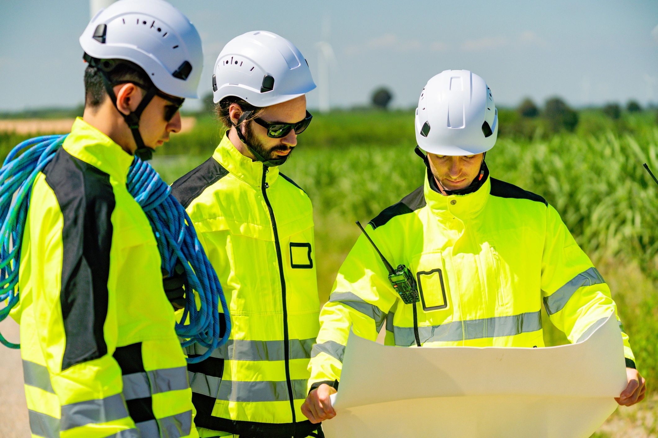 Three engineers in helmets and high-visibility jackets reviewing plans outdoors.