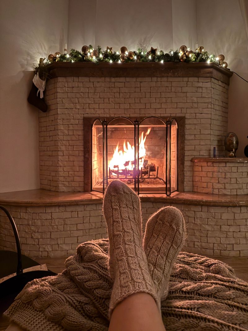 Cozy mood on Christmas Eve with fire in fireplace, Christmas tree. Women's feet in cozy wool socks warming up by fireplace