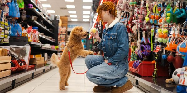 Woman in denim jacket playing with her dog in a pet store aisle.