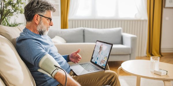 Man monitoring blood pressure during virtual visit at home.