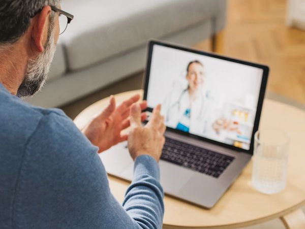 Man having a telehealth consultation with a doctor on a laptop at home.