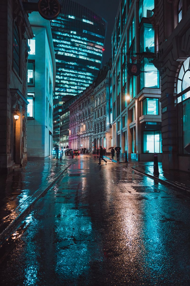 People walking on a wet cobblestone street reflecting neon lights in the city of london at night