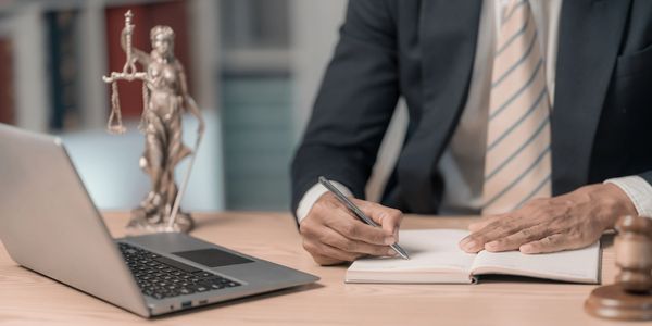 A man in a suit writes in a notebook with legal symbols nearby.
