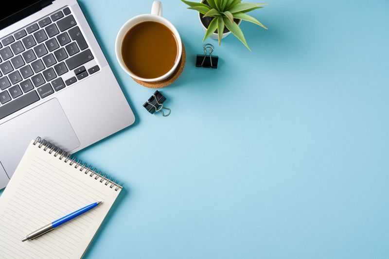 Coffee cup, laptop keyboard and various stationery items on blue office desk. Business office concept