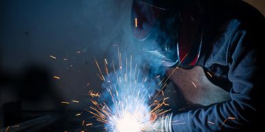 A welder working with sparks flying around in a dark environment.