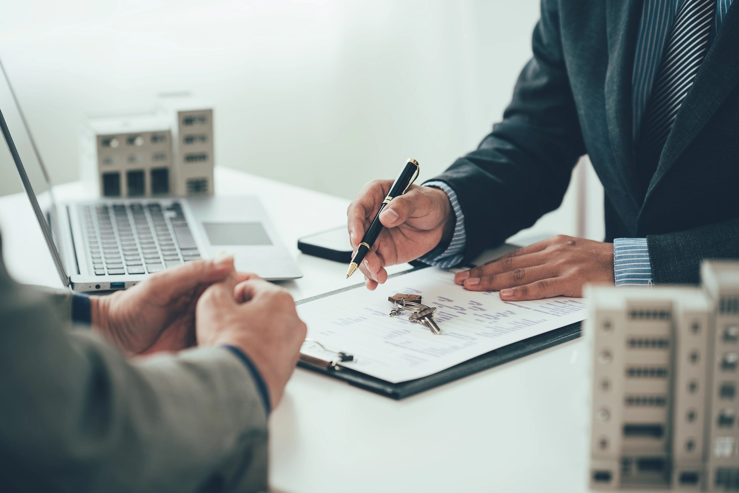 Real estate agent discussing property details with client and pointing at contract with keys on table.