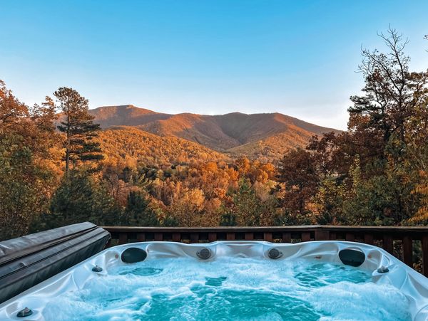 Hot tub on a deck overlooking autumn mountains at sunset.