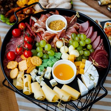 A colorful charcuterie board with meats, cheeses, grapes, crackers, and mustard.