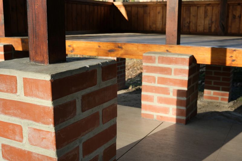 Sunlight bathes the sturdy brick columns supporting a wooden deck.