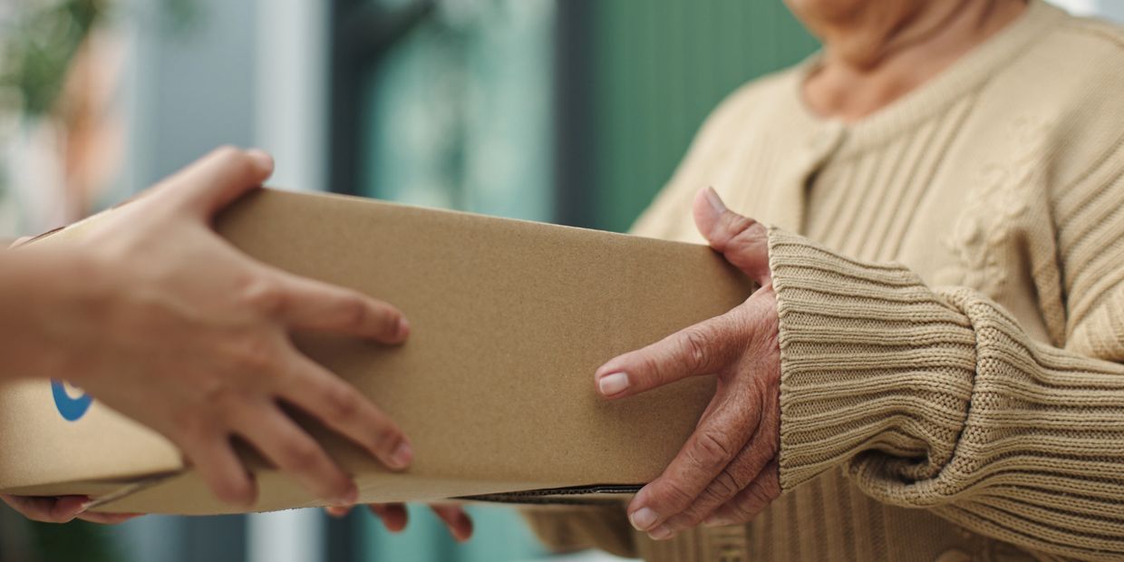 An elderly person receiving a cardboard package from another individual.