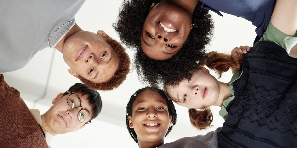 "Diverse group of young children and teens standing in a circle, engaging in a support