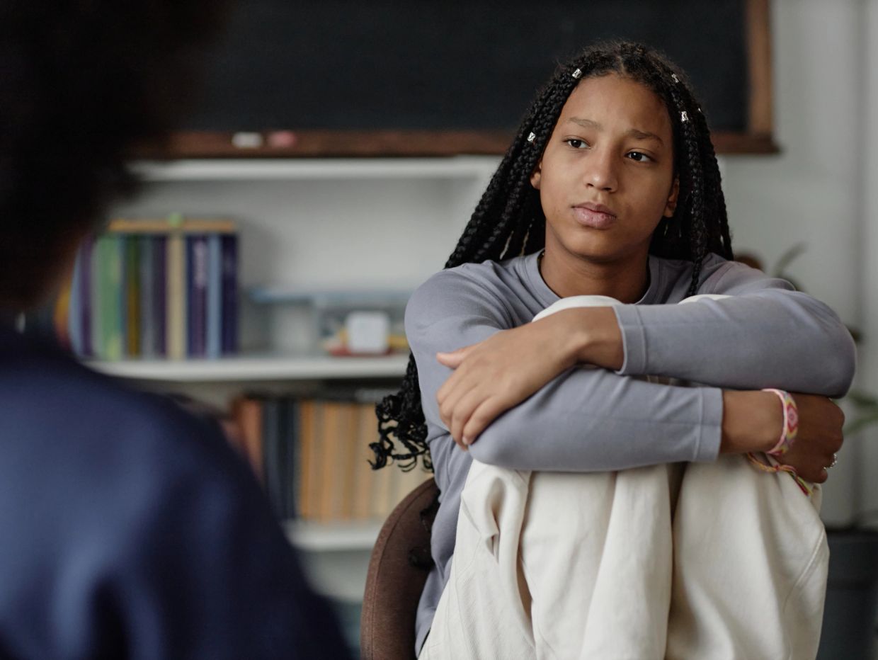 Teen girl sitting with knees hugged, looking thoughtful.
