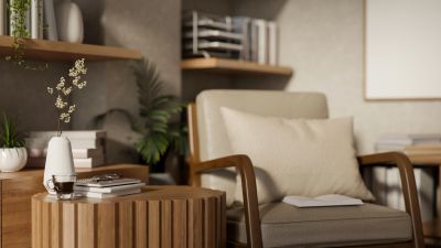 Cozy beige armchair next to a round wooden table with books and a vase.