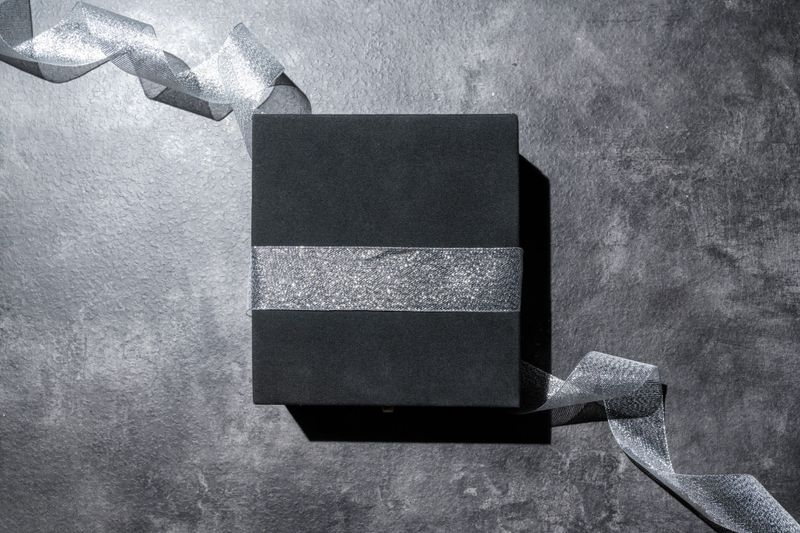 Top view of the black gift box wrapped with silver ribbon on the table. Mockup or copy space. Concept of decoration for holidays, anniversaries, celebrations, presents, or surprises. Flat lay