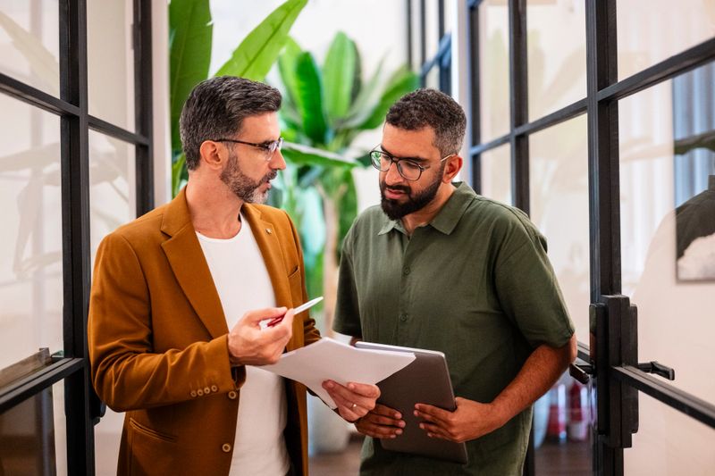 Male business professionals in their 30s in modern office, talking and concentrating