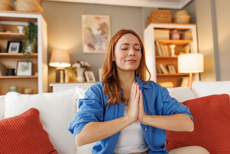 Young woman practicing mindfulness meditation on comfortable sofa in her living room, finding inner peace and relaxation in the comfort of her home