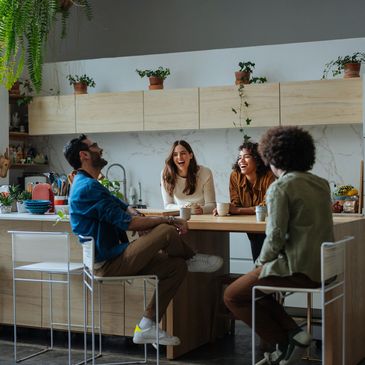 Four friends laughing and enjoying coffee together in a modern kitchen.