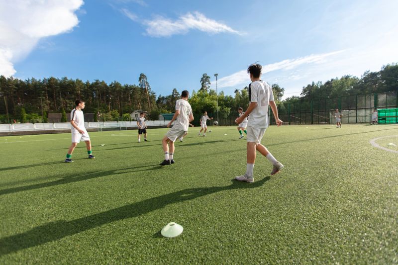 A group of young people play football on a field against a blue sky. The scene is energetic and competitive