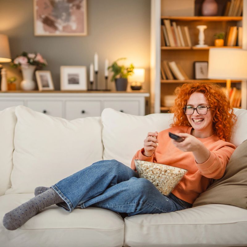 happy adult woman watch movie on sofa and eat popcorn leisure activity