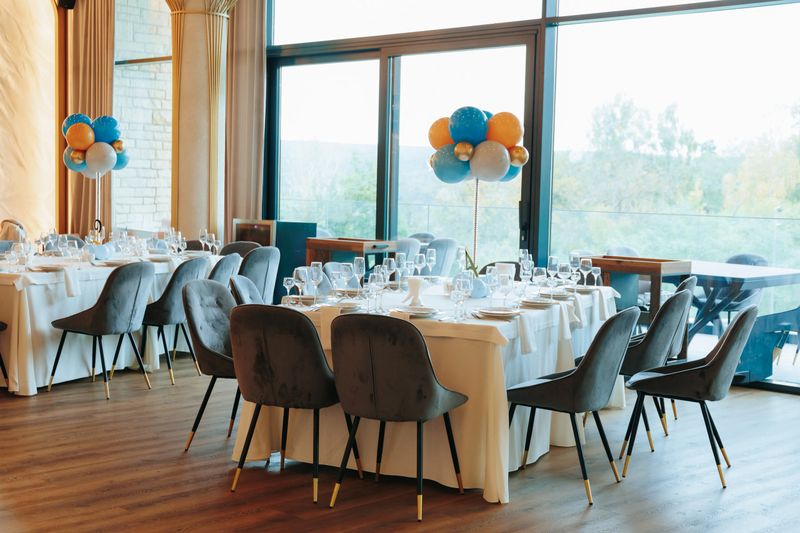 Elegant banquet setup featuring a vibrant balloon centerpiece, refined table settings, and panoramic views through large windows, creating a luxurious and festive atmosphere.