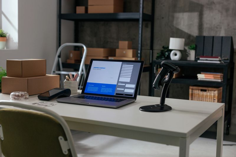 A neat workspace showing a laptop open on a standing desk, with various parcels and a lamp
