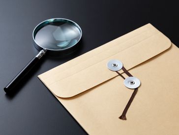 Magnifying glass beside a closed brown envelope on a black surface.
