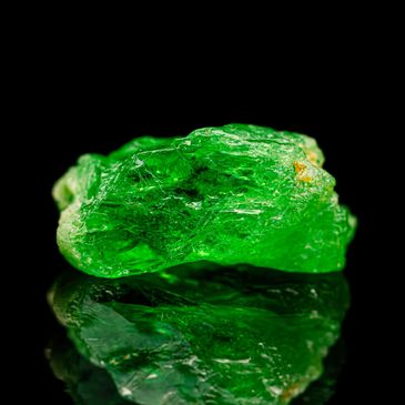 Vibrant green crystal with detailed texture on black reflective surface.