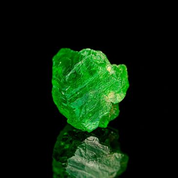 A vibrant green crystal with a textured surface on a reflective black background.