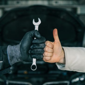 Two hands showing a thumbs up and holding a wrench, symbolizing teamwork.