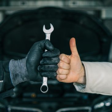 Two hands holding a wrench with a thumbs-up gesture.