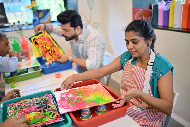 In a bright studio, vibrant fluid art session at an art workshop, featuring participants enthusiastically pouring and blending colorful paints on canvases, surrounded by splashes of vivid hues and creative energy