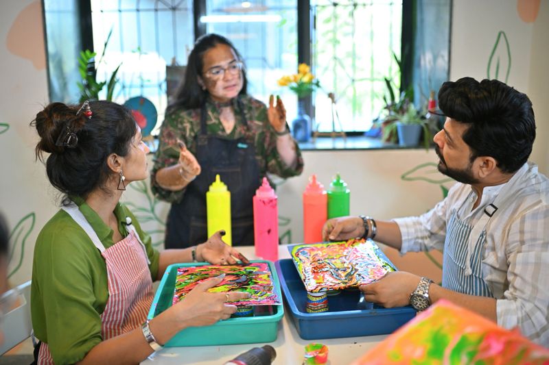 A passionate woman artisan guides a mid-adult couple at a creative fluid art session in a vibrant studio, offering personalized instructions as they experiment with colorful paints and explore new artistic techniques.