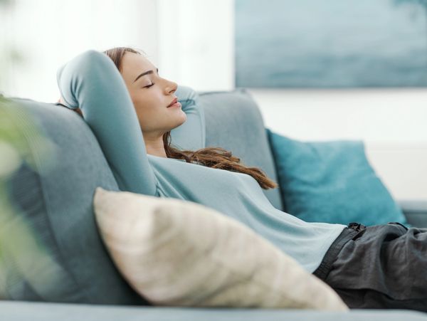 A woman relaxes on a blue couch with her eyes closed, enjoying a peaceful moment.