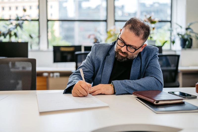 Handsome mid-adult man writing in a notebook at the desk in the office building in Sydney in Australia.
