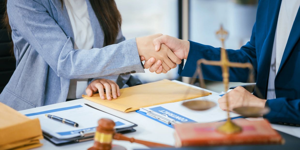 Two professionals shaking hands over a legal contract at a desk.