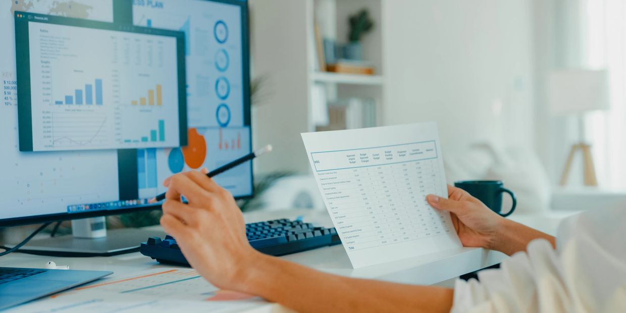 Person analyzing financial charts and data at a computer desk.