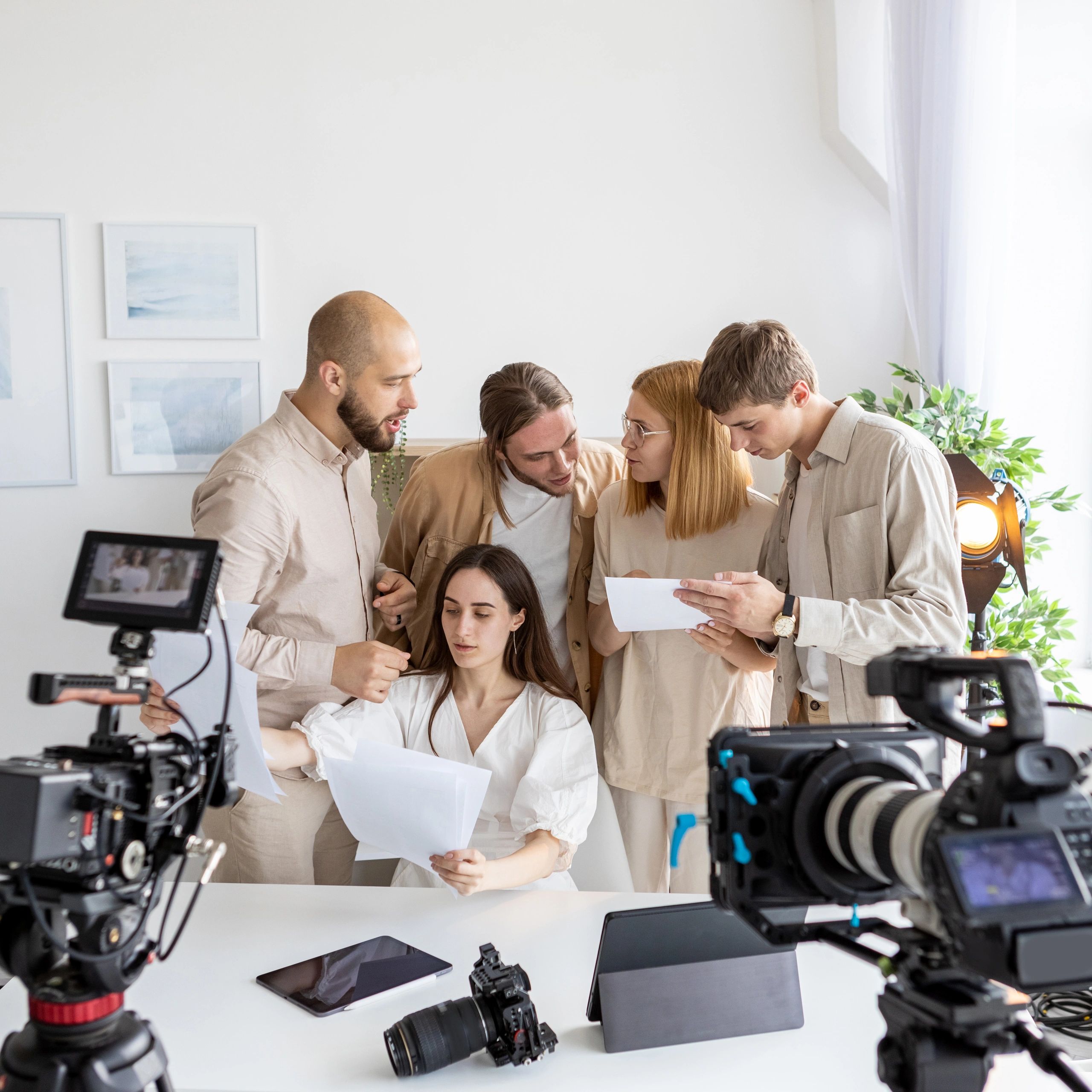 A group of young filmmakers reviewing a script on set with professional cameras.