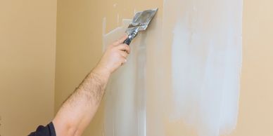 Person applying white paint or primer on a wall with a putty knife.