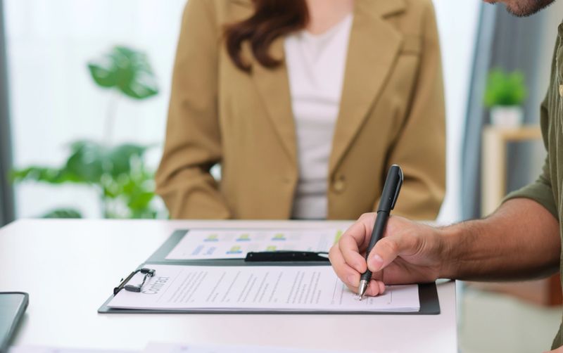Asian couple reviewing and sign contract financial documents with the guidance of  advisor at home,collaboration and thoughtful planning for financial success