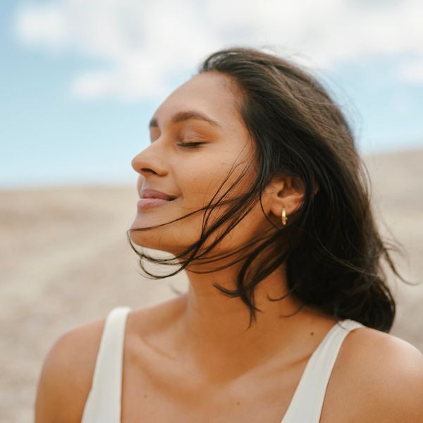 Woman enjoying a peaceful moment outdoors with eyes closed and hair blowing.