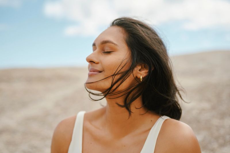 A portrait of a young woman  outdoors enjoying a calming breeze moving her hair against a blue sky and natural background
