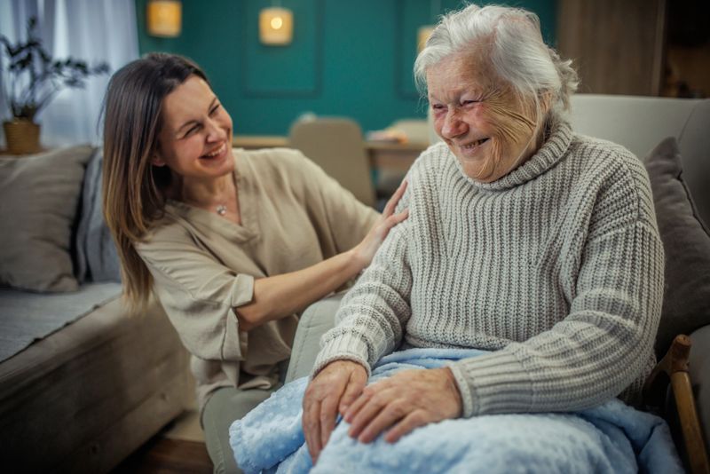 Cheerful mature woman embracing senior mother at home and looking away. Portrait of elderly mother and middle aged daughter smiling together