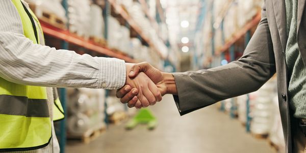 Two workers shaking hands in a warehouse setting.